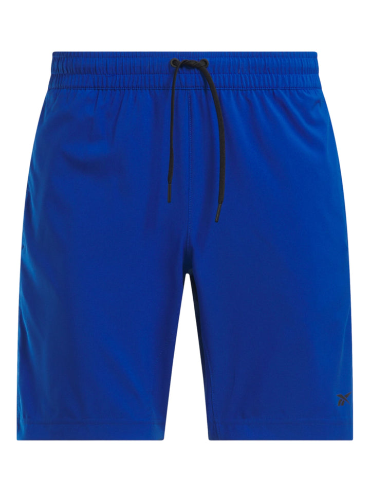 Hombre vistiendo shorts deportivos color azul marca Reebok con camiseta azul marino y tenis blancos.