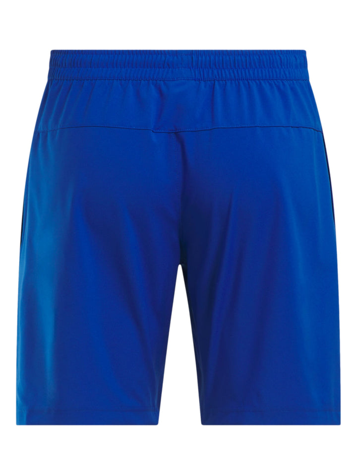 Hombre vistiendo shorts deportivos color azul marca Reebok con camiseta azul marino y tenis blancos.