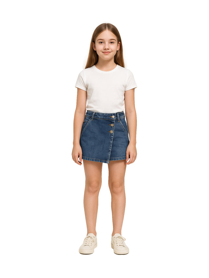 Niña vistiendo una falda corta de mezclilla azul con botones frontales y camiseta blanca.