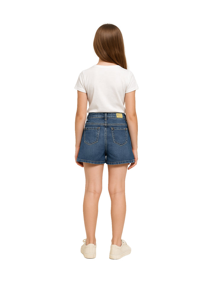 Niña vistiendo una falda corta de mezclilla azul con botones frontales y camiseta blanca.