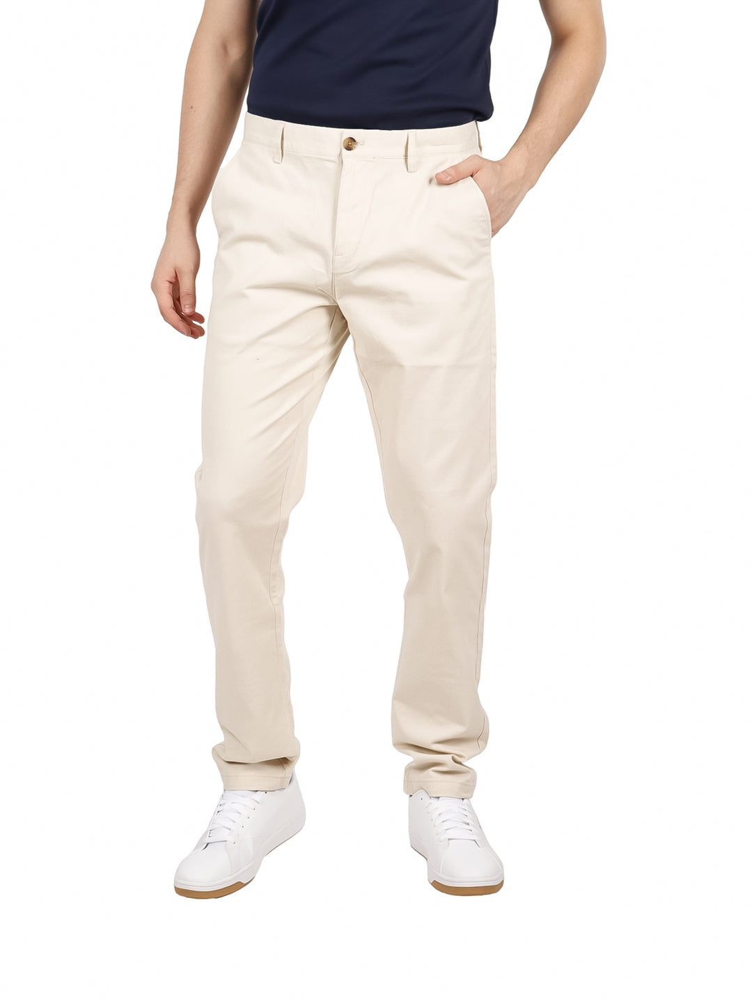 Hombre vistiendo pantalones chinos de color beige y tenis blancos sobre fondo blanco.