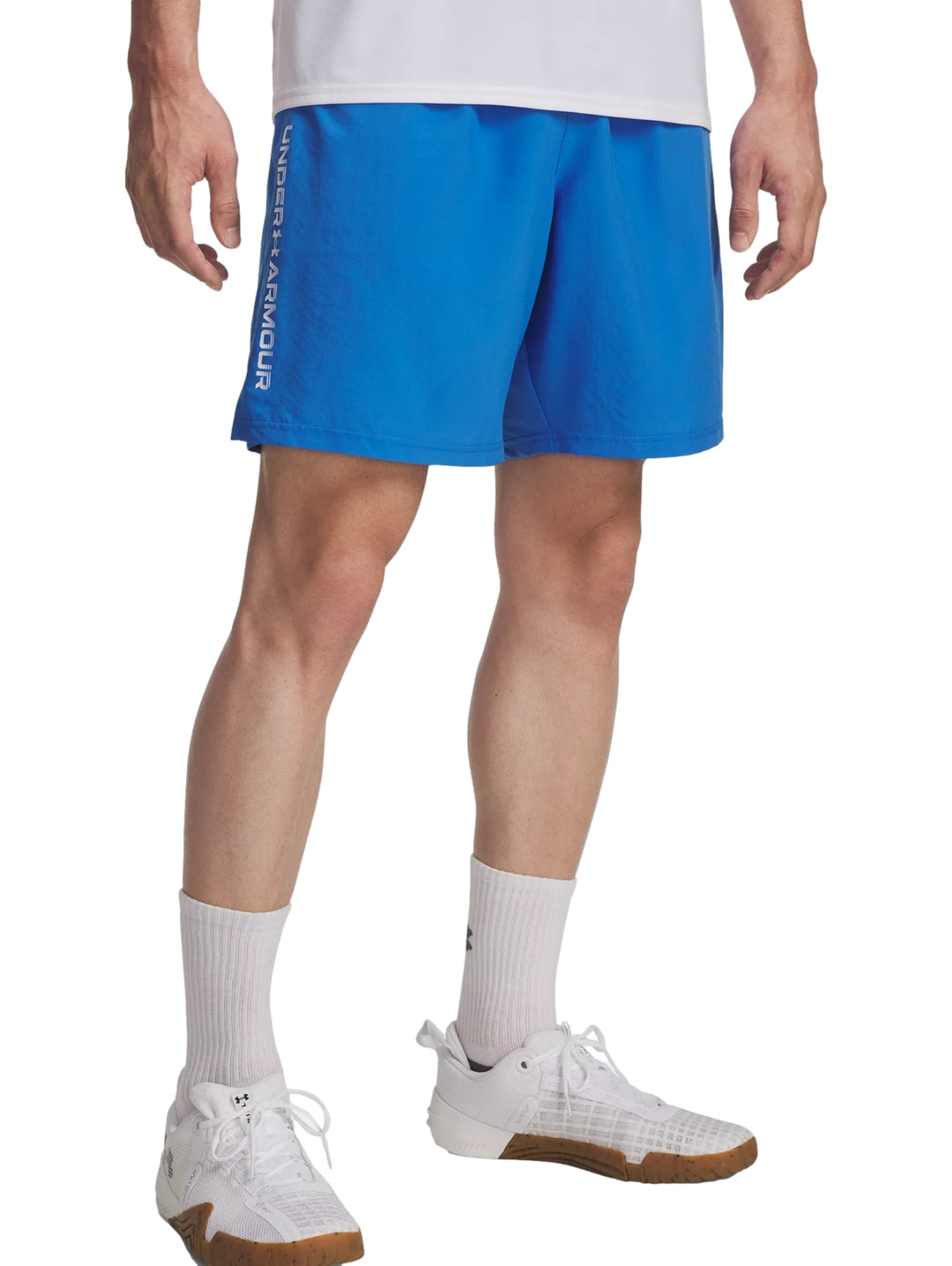 Hombre vistiendo shorts deportivos color azul de la marca Under Armour con logotipo lateral blanco.