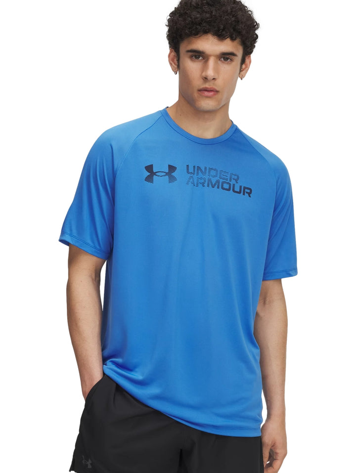 Hombre vistiendo una camiseta deportiva azul de manga corta con logo reflectante de Under Armour en el pecho.
