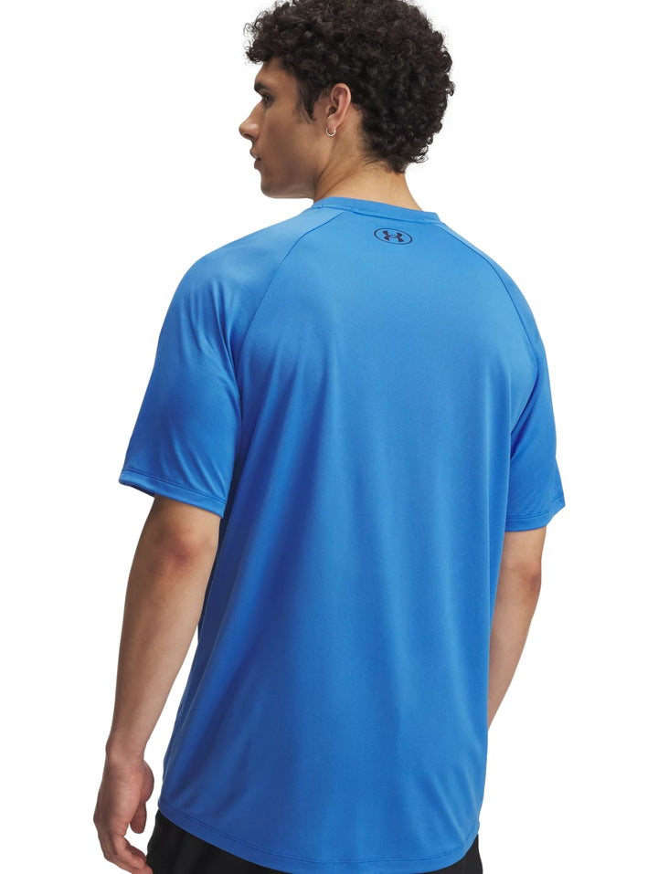 Hombre vistiendo una camiseta deportiva azul de manga corta con logo reflectante de Under Armour en el pecho.