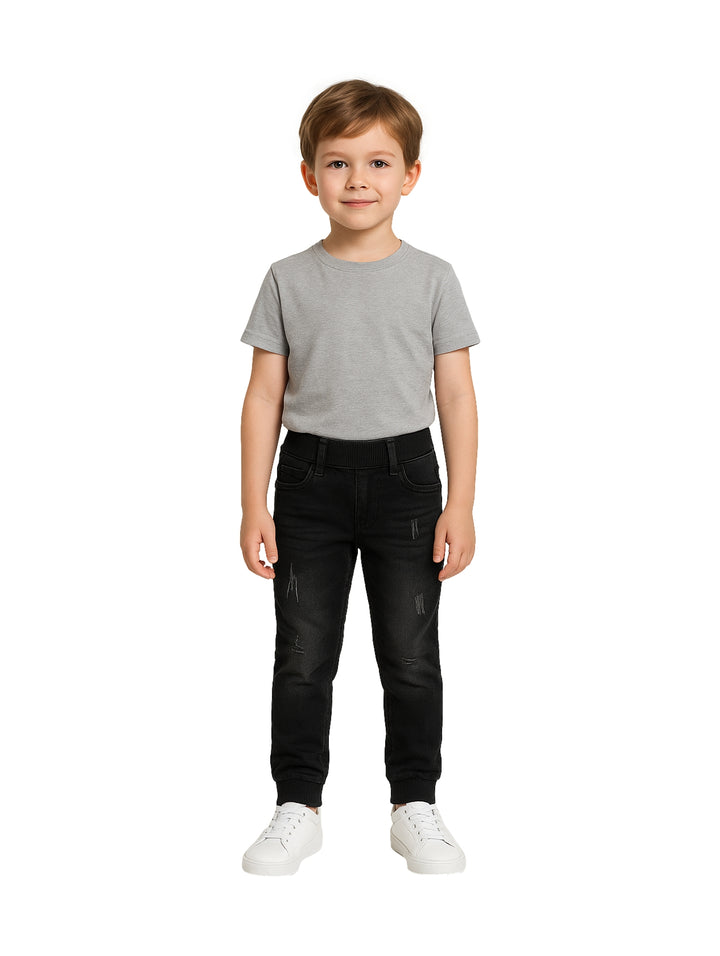 Niño vistiendo pantalón negro casual con detalles desgastados y camiseta gris.