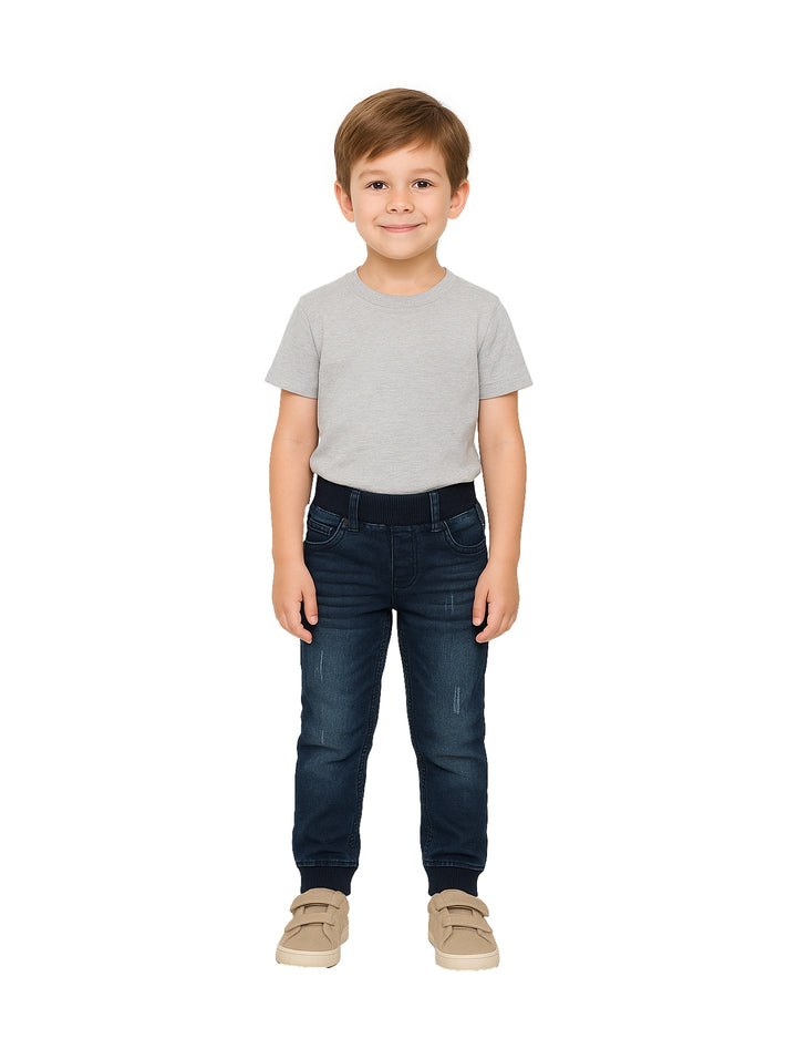Niño modelando un pantalón de mezclilla azul oscuro con cintura elástica.