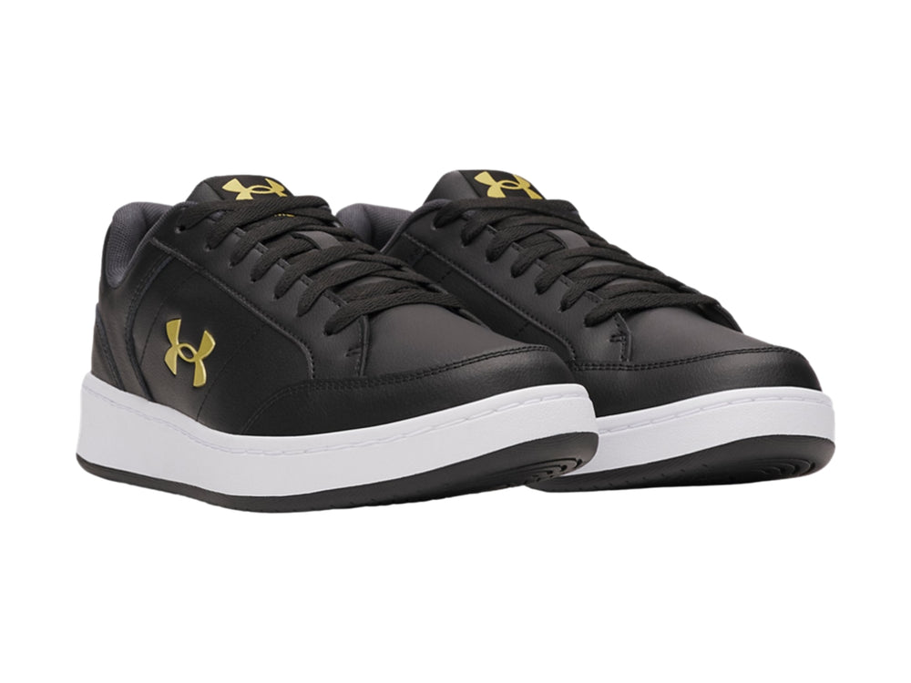 Tenis Under Armour color negro con suela blanca y logotipo dorado en el lateral.
