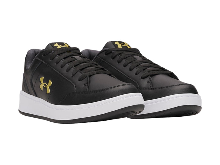 Tenis Under Armour color negro con suela blanca y logotipo dorado en el lateral.