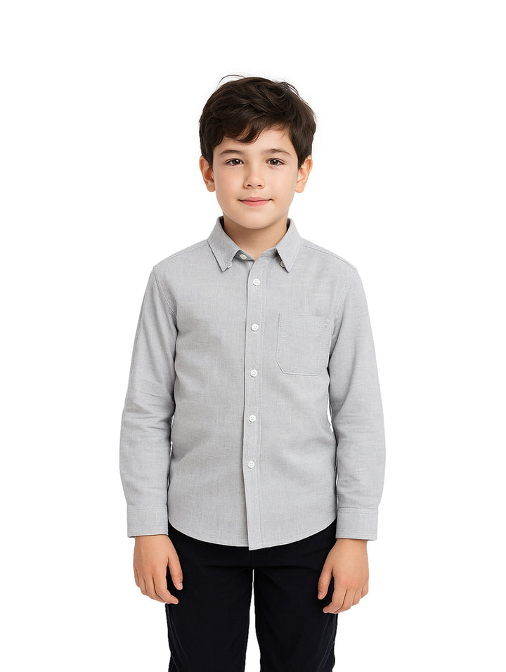 Niño vistiendo una camisa gris de manga larga con botones y pantalones azul marino.