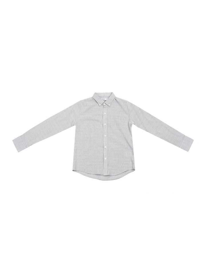 Niño vistiendo una camisa gris de manga larga con botones y pantalones azul marino.