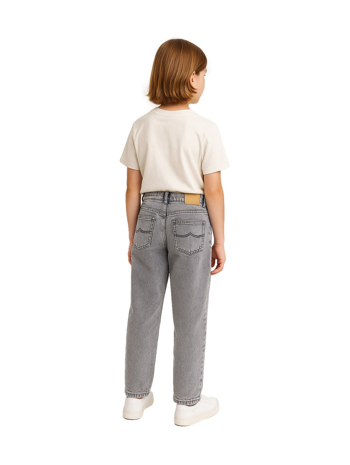 Niño vistiendo un pantalón vaquero color gris de corte recto y camiseta blanca.