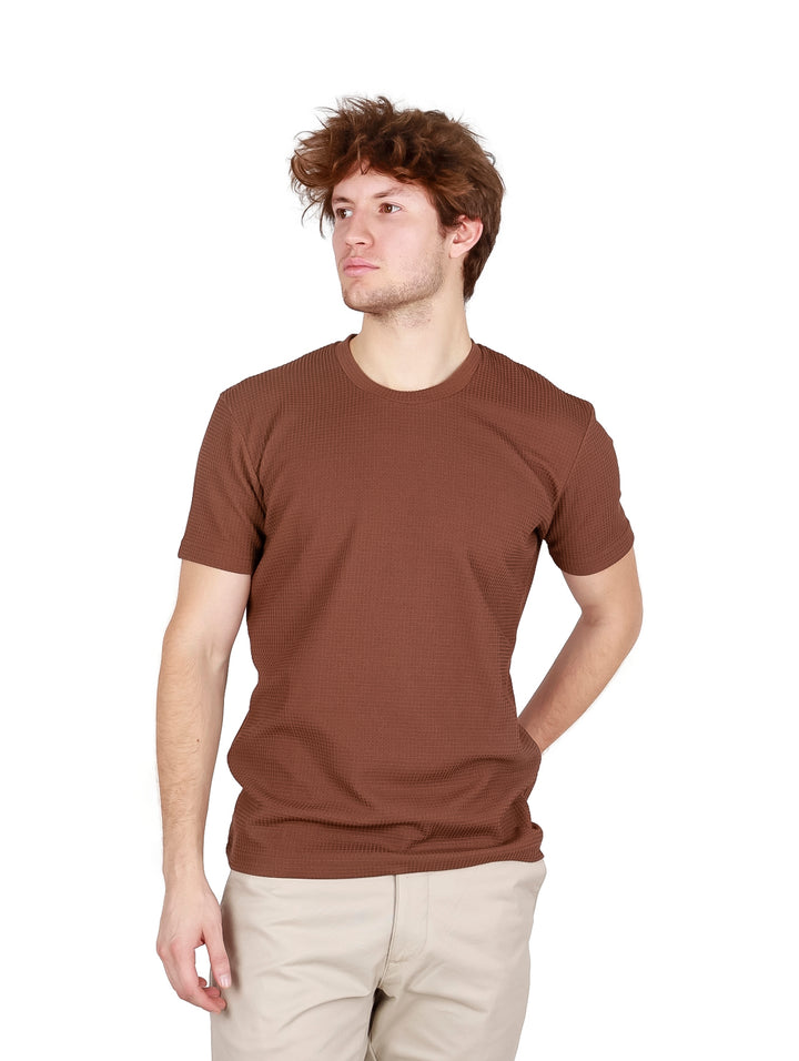 Hombre vistiendo una playera de manga corta color café con textura y cuello redondo.
