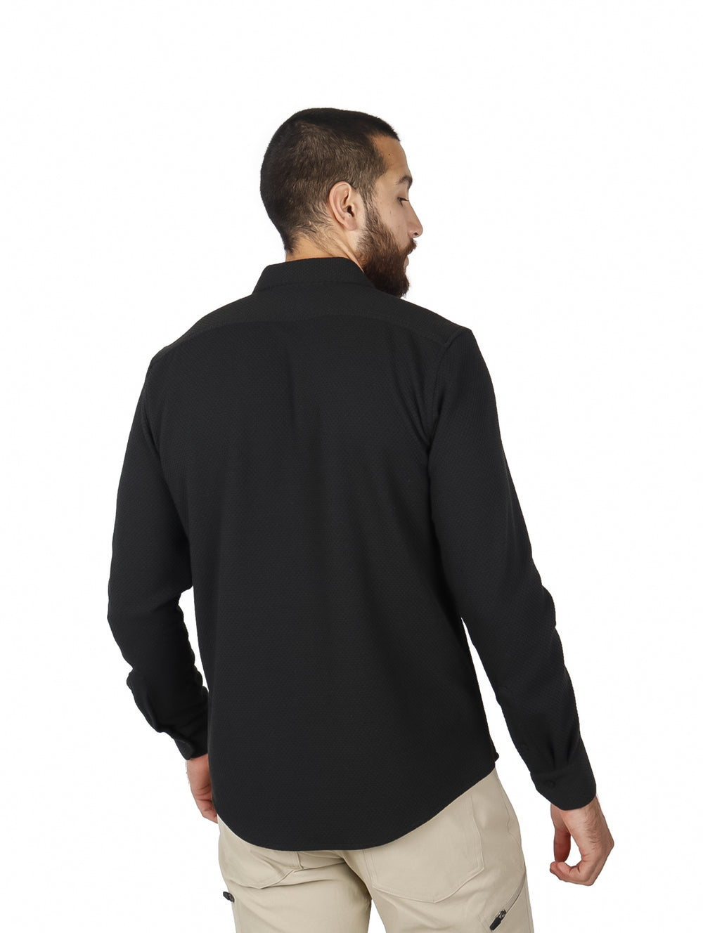 Hombre vistiendo una camisa negra de manga larga con botones y pantalones beige.