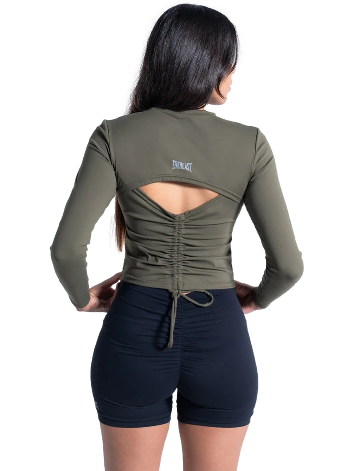 Mujer vistiendo playera deportiva manga larga color olivo de corte corto y shorts negros.