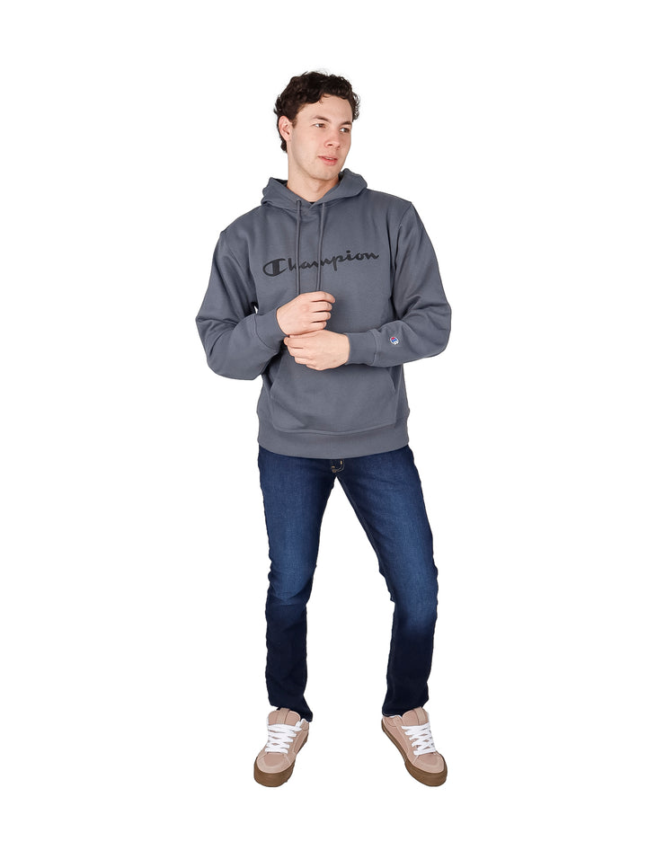 Hombre vistiendo una sudadera con capucha color gris oscuro de la marca Champion con logotipo en el pecho.