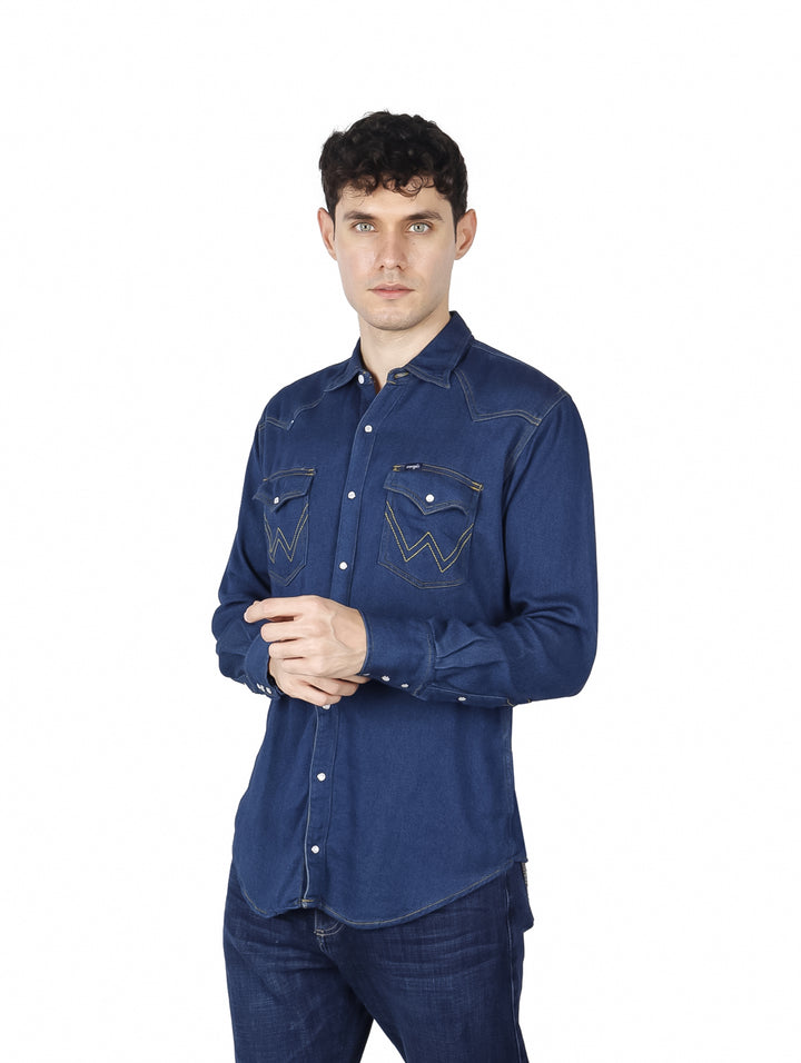 Hombre vistiendo una camisa de mezclilla color índigo de manga larga con bolsillos frontales.
