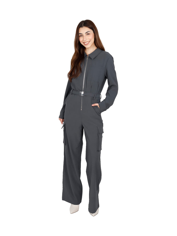 Mujer vistiendo un jumpsuit gris con cierre frontal, bolsillos cargo y cinturón a juego sobre fondo blanco.
