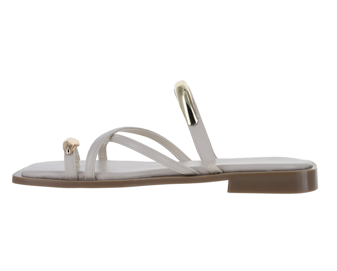 Sandalias planas color latte con detalles metálicos dorados y diseño de tiras cruzadas.
