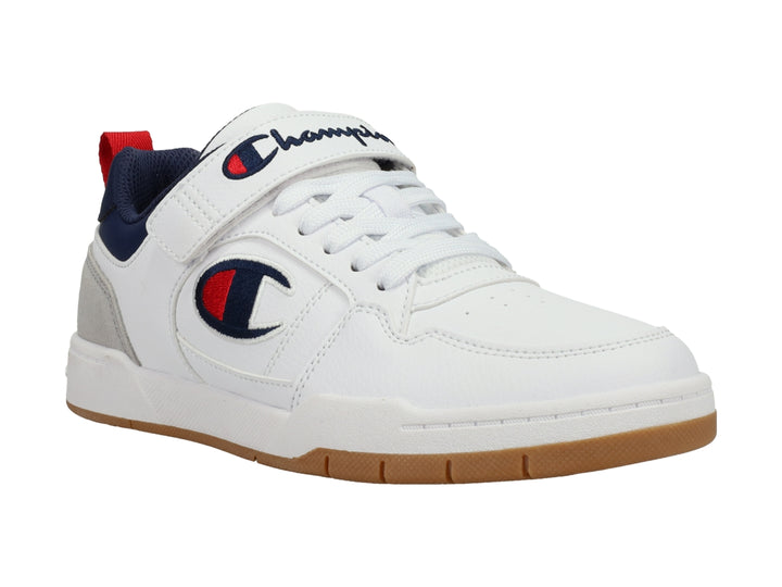 Tenis Champion blancos con detalles en gris y azul marino, correa ajustable y suela color caramelo.