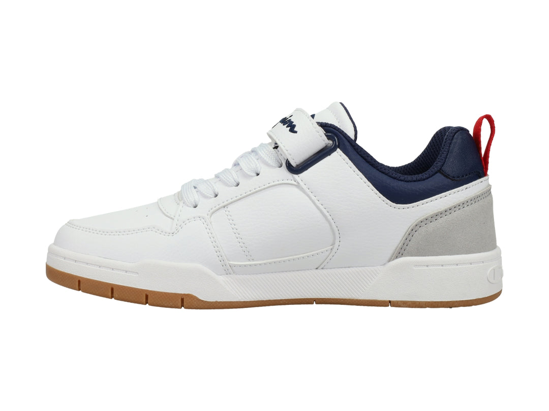 Tenis Champion blancos con detalles en gris y azul marino, correa ajustable y suela color caramelo.