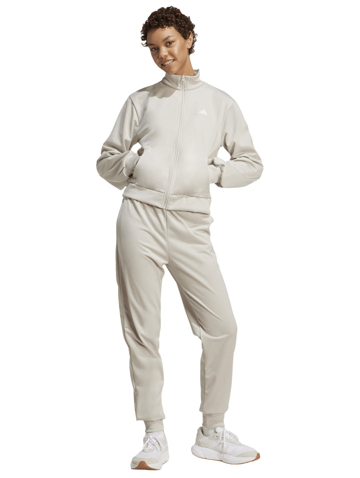 Conjunto deportivo Adidas Essentials Feel Cozy en color beige, compuesto por chaqueta y pantalón para mujer.