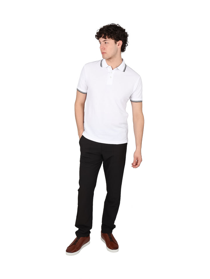 Hombre vistiendo una playera polo blanca con detalles negros en el cuello y los bordes de las mangas.