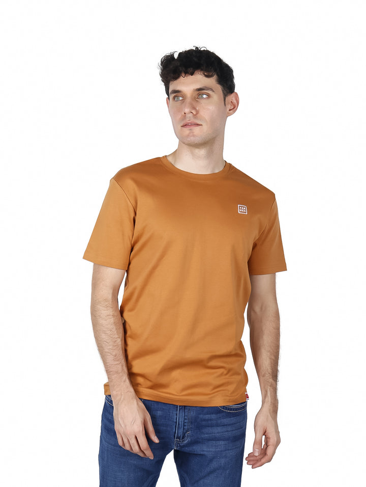 Hombre vistiendo una playera de manga corta color marrón con un pequeño logo blanco en el pecho.