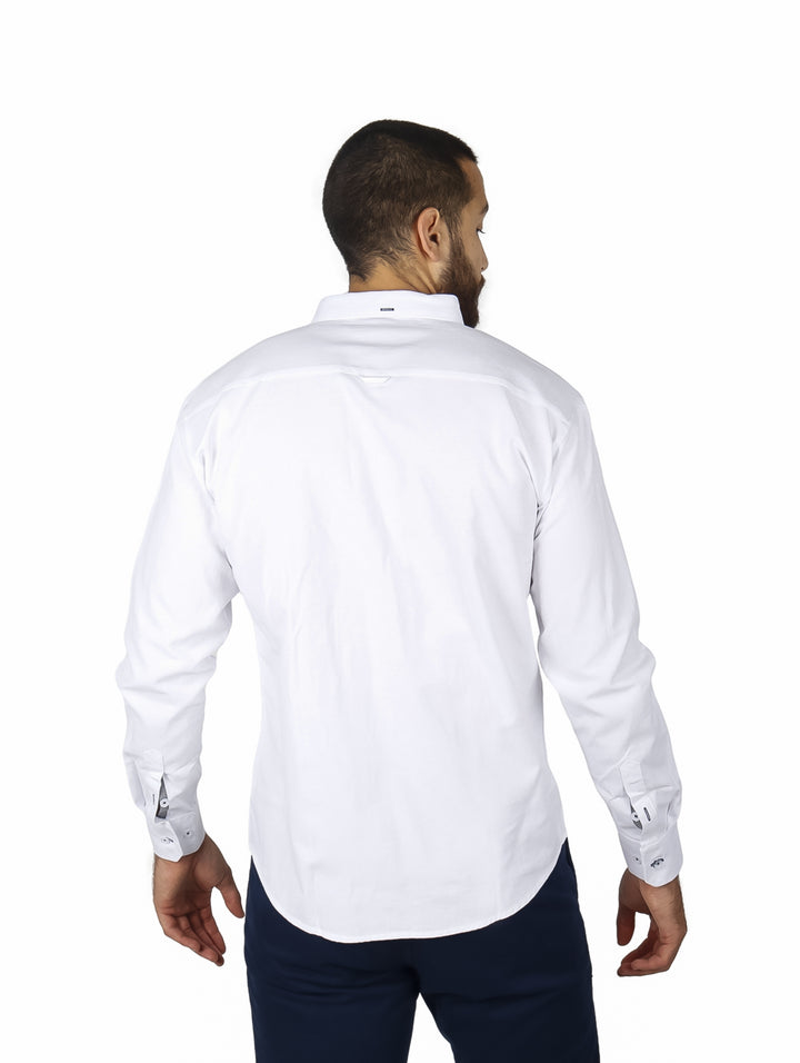 Hombre vistiendo camisa blanca de manga larga con detalle de rayas rojas y azules en el pecho.