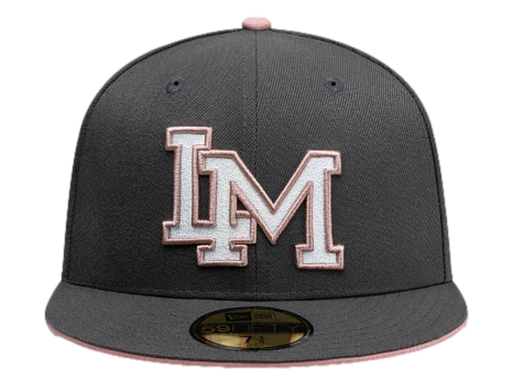 Gorra New Era color gris oscuro con visera plana y letras bordadas en blanco y rosa en el frente.