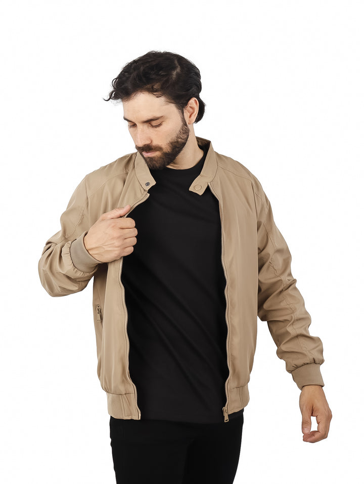Hombre usando una chamarra tipo bomber de color beige con camiseta negra.