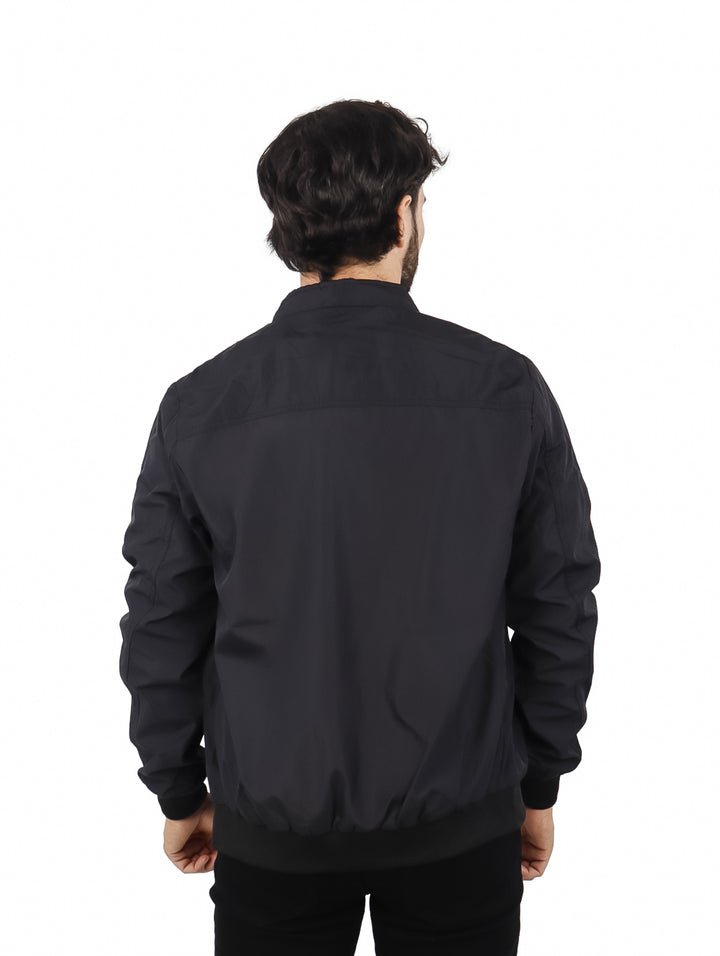 Hombre vistiendo una chamarra tipo bomber color negro sobre una playera azul.
