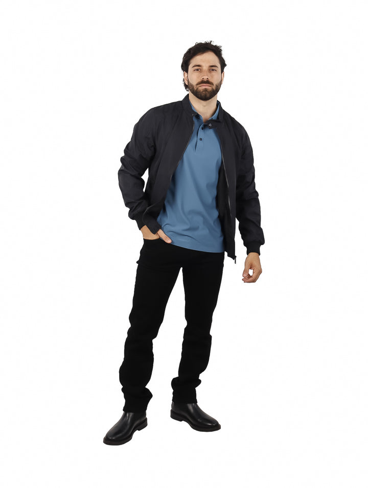 Hombre vistiendo una chamarra tipo bomber color negro sobre una playera azul.