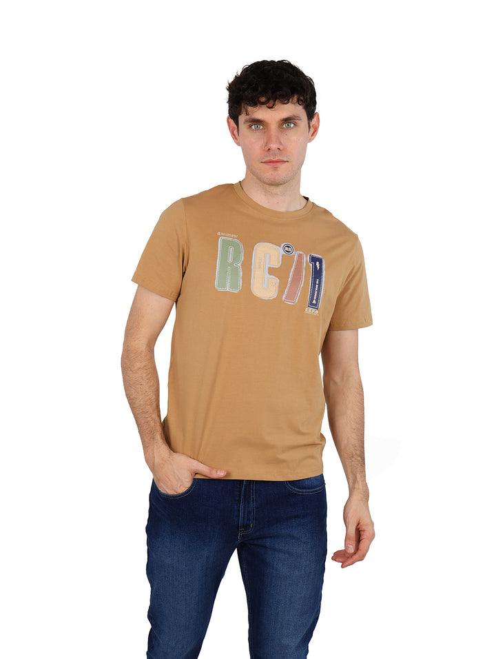 Hombre vistiendo playera de manga corta color café con estampado frontal y jeans azules.