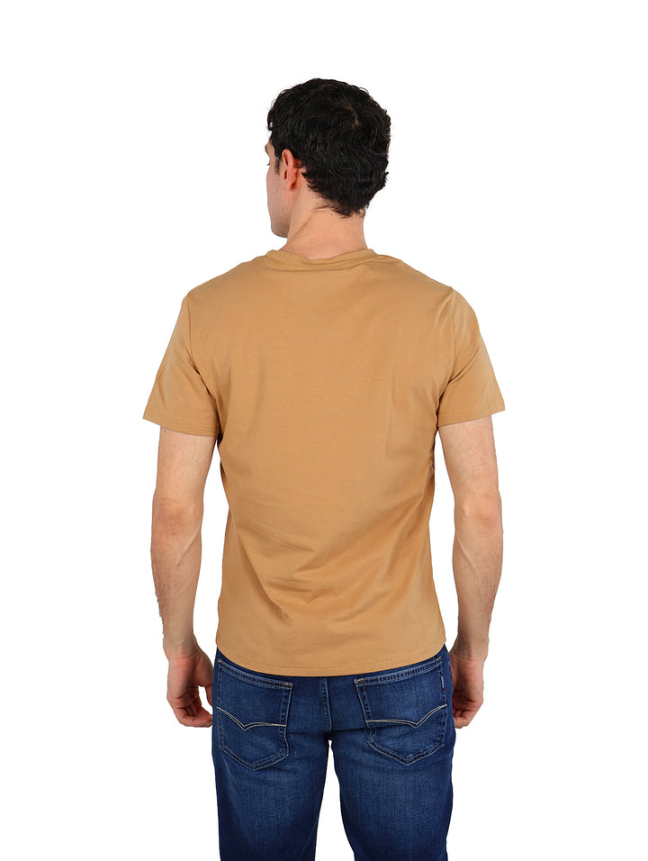 Hombre vistiendo playera de manga corta color café con estampado frontal y jeans azules.