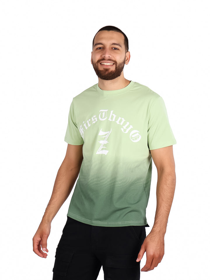 Hombre vistiendo playera verde con efecto degradado y estampado blanco en el pecho.