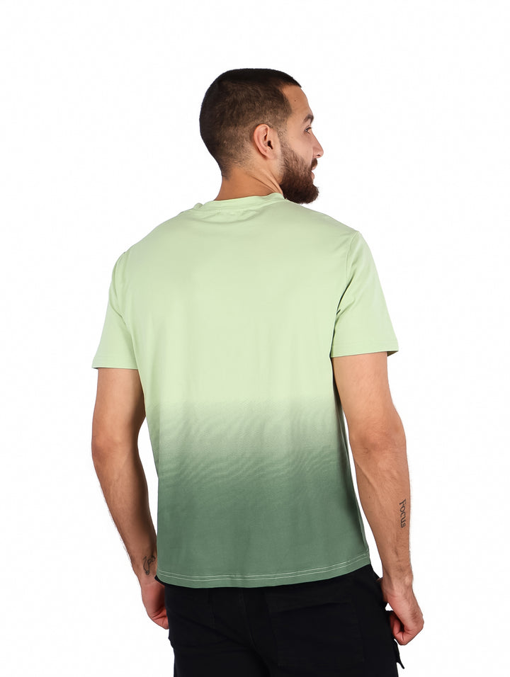 Hombre vistiendo playera verde con efecto degradado y estampado blanco en el pecho.