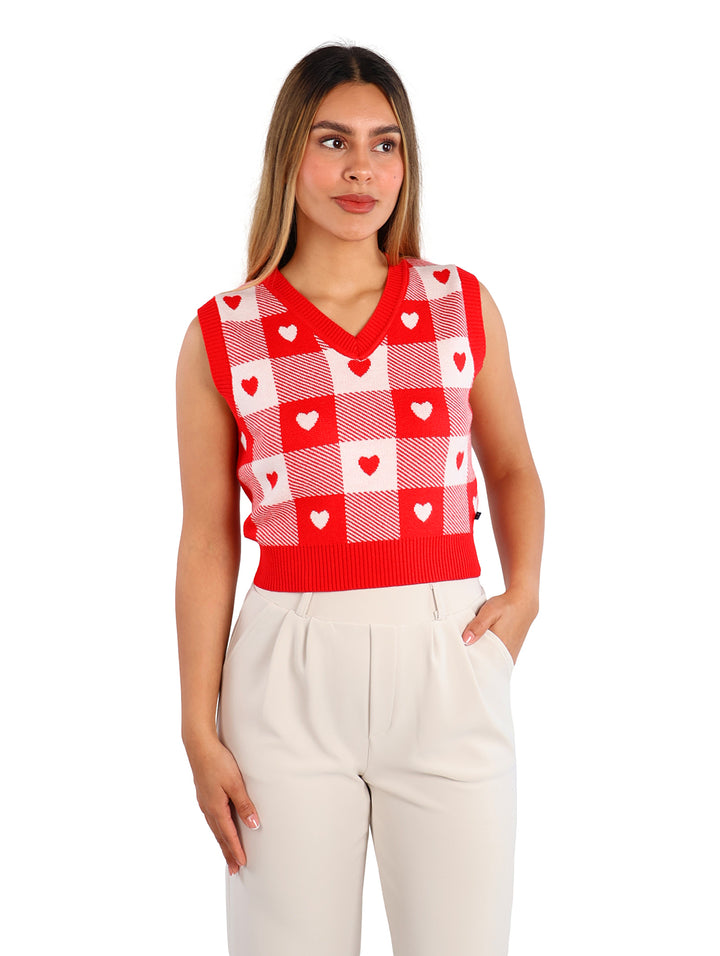 Mujer vistiendo un chaleco de punto rojo y blanco con estampado de cuadros y corazones, cuello en V.