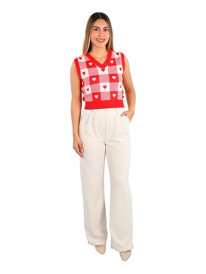 Mujer vistiendo un chaleco de punto rojo y blanco con estampado de cuadros y corazones, cuello en V.