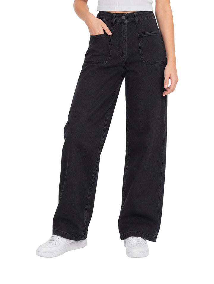 Mujer vistiendo pantalones Losan de denim negro, corte ancho y talle alto con tenis blancos.