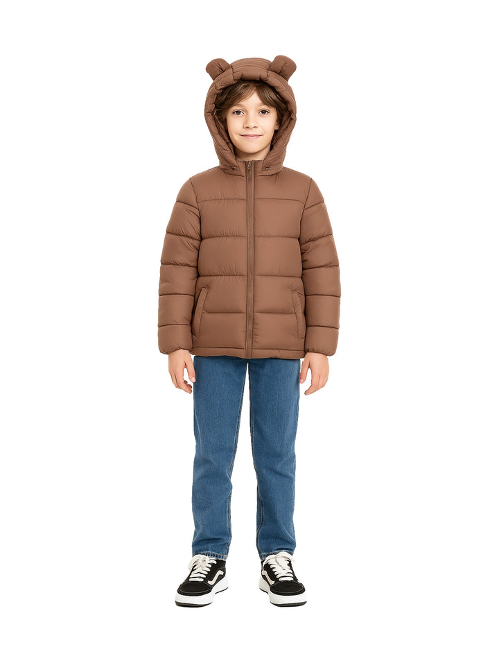 Niño vistiendo chamarra acolchada color café con capucha que tiene orejas de oso, jeans azules y tenis negros.