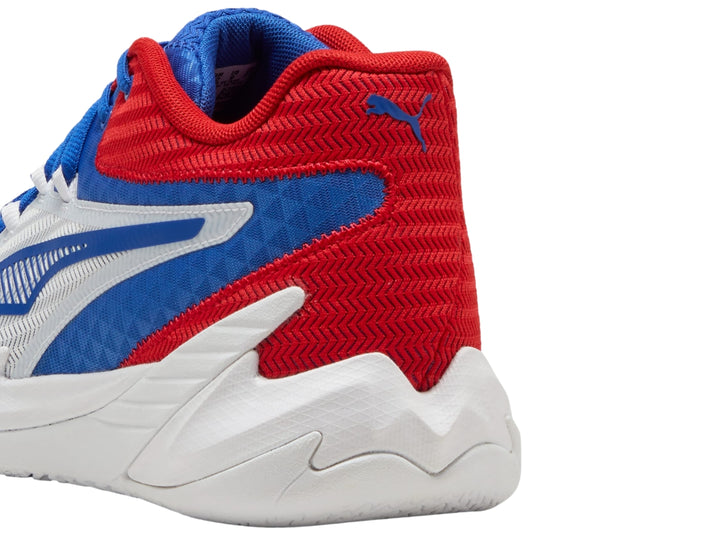 Tenis de baloncesto PUMA en colores blanco, rojo y azul con suela blanca y diseño moderno.