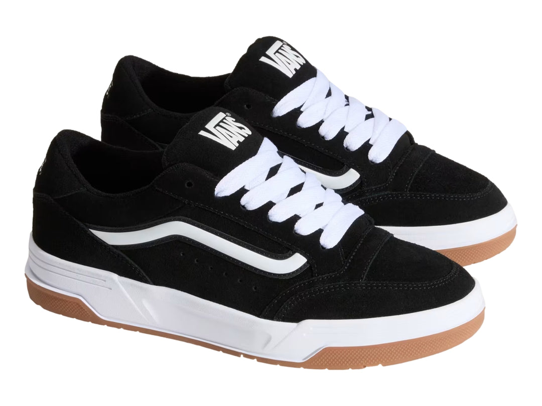 Tenis Vans color negro con franja blanca, suela blanca y base de goma color marrón.