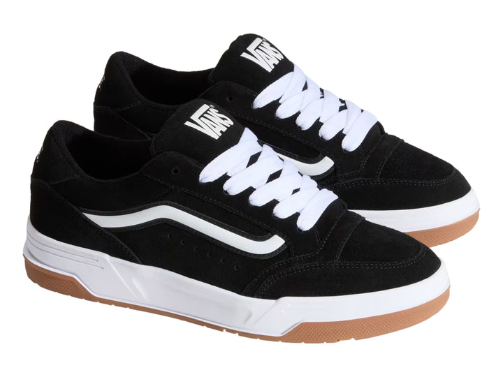 Tenis Vans color negro con franja blanca, suela blanca y base de goma color marrón.