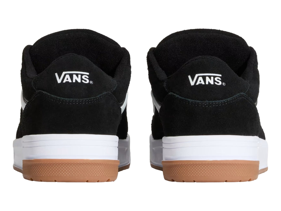 Tenis Vans color negro con franja blanca, suela blanca y base de goma color marrón.