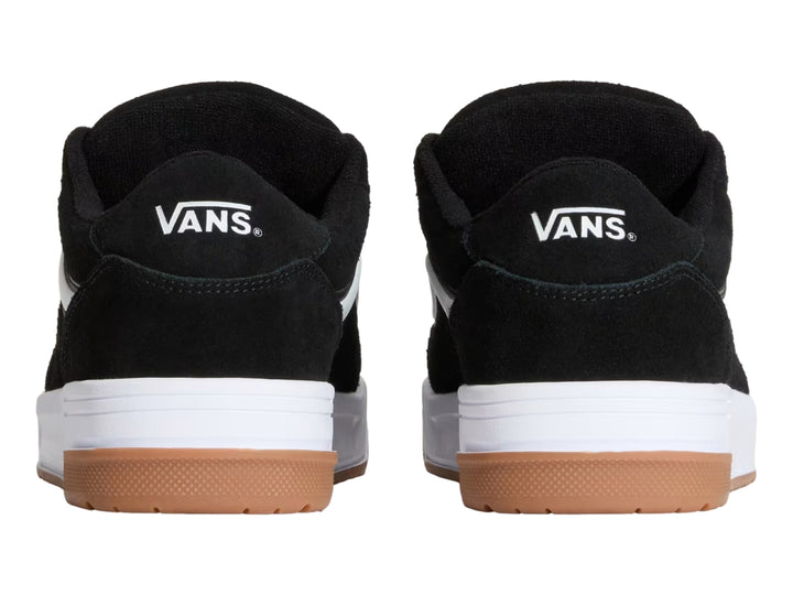 Tenis Vans color negro con franja blanca, suela blanca y base de goma color marrón.
