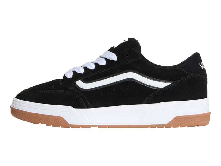 Tenis Vans color negro con franja blanca, suela blanca y base de goma color marrón.