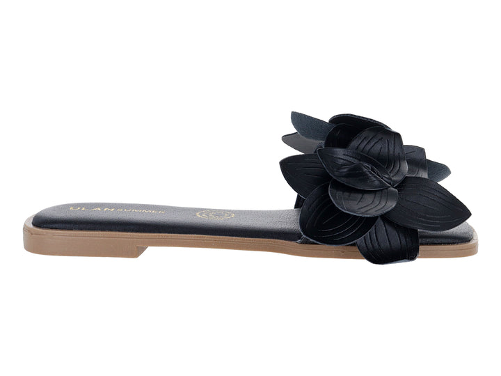 Sandalia plana color negro con un adorno de flor grande en la correa superior.
