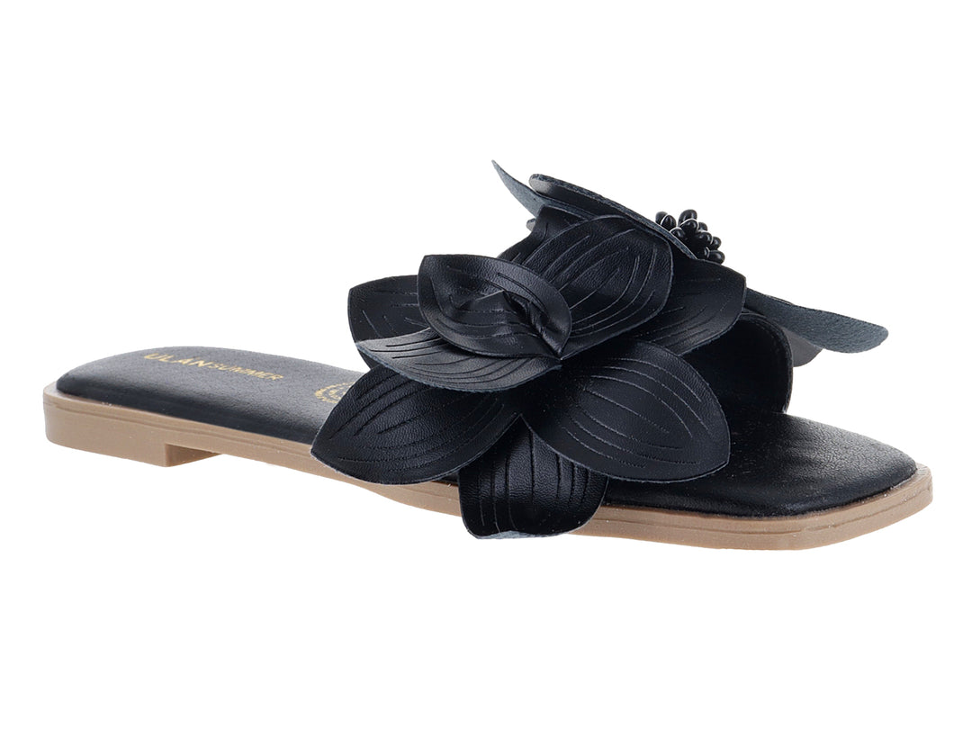 Sandalia plana color negro con un adorno de flor grande en la correa superior.