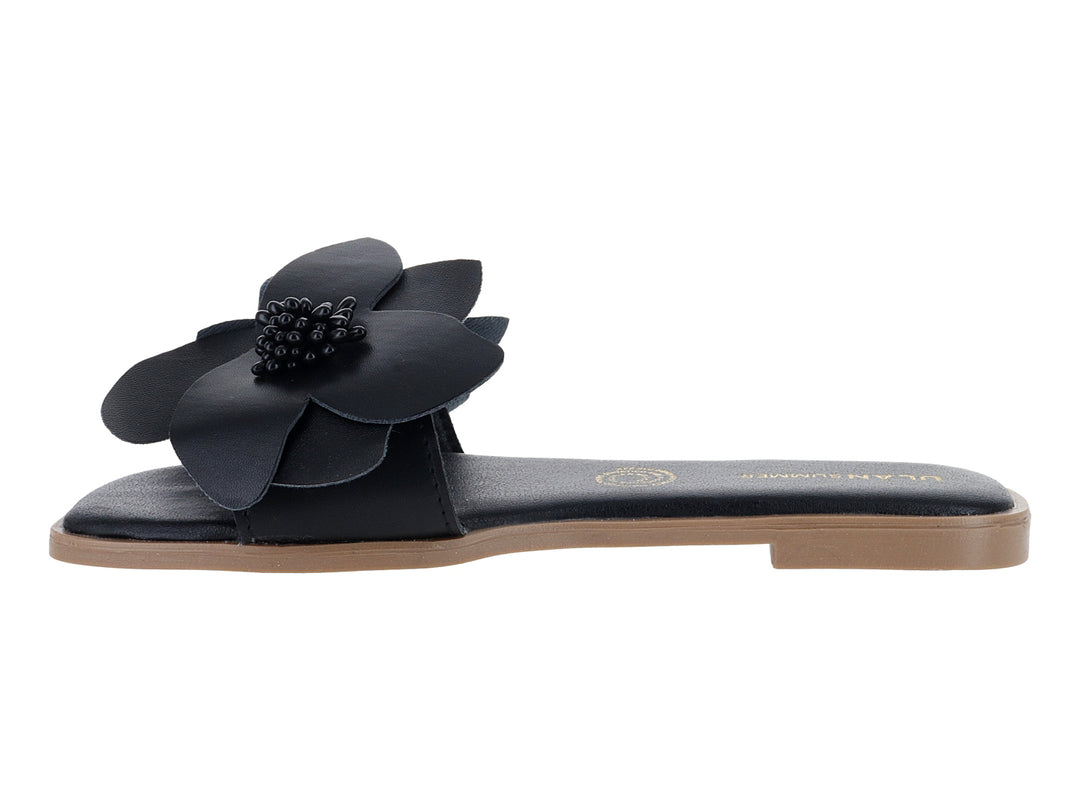 Sandalia plana color negro con un adorno de flor grande en la correa superior.