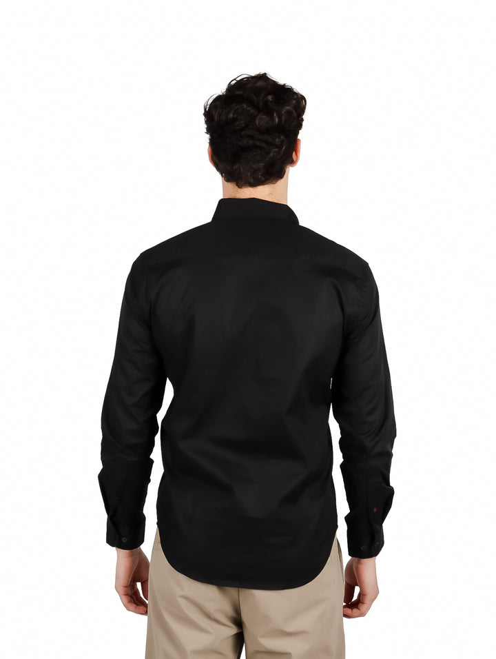 Hombre vistiendo una camisa lisa de color negro con manga larga y cuello, estilo elegante.